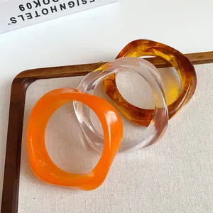 Close-up of three irregular acrylic bangles in orange, clear, and amber marbled patterns
