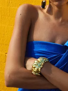 Close-up view of a golden irregular pleated wide cuff bracelet styled on a model's wrist