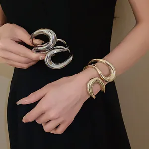 Close-up of chunky irregular geometric hollow open bangles in gold and silver finish