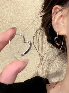 Close-up detail of minimalist silver heart-shaped hoop earrings worn on ear and held in hand