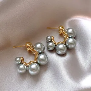 Nahaufnahme französischer Creolen in Gold mit grauen Perlen auf elegantem Satin