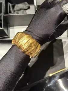Detailed view of chunky irregular pleated gold bangle worn over black satin luxury gloves.