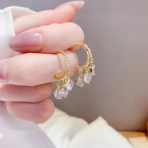 Primer plano de aros en C dorados con brillantes detalles de circonitas colgantes.