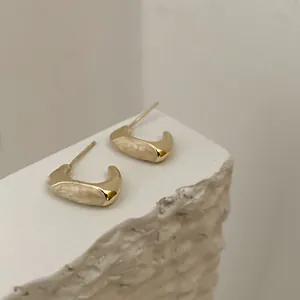 Primer plano de pendientes dorados en forma de C con elegante esmalte en color crema