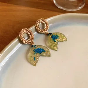 Detailed view of gold textured earrings with resin mermaid tail and blue glitter flakes