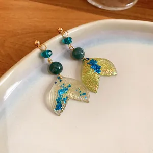 Close-up detail of mermaid tail earrings with blue crystals and green beads