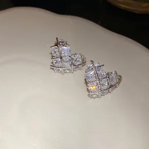 Close-up of heart-shaped zircon earrings with square-cut crystals and silver cage design