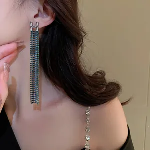 Close-up of long tassel earrings with rhinestone letter H and blue crystals on model.