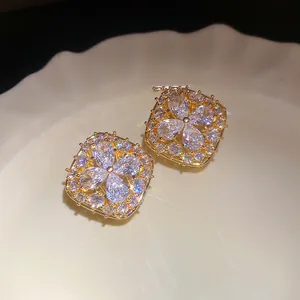 Macro shot of elegant square gold-tone stud earrings with sparkling floral zircon center