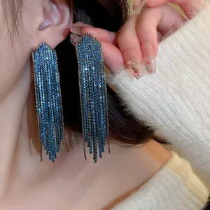 Close-up view of glamorous long blue rhinestone tassel dangle earrings worn by a model
