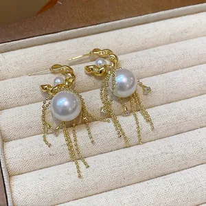Close-up of elegant gold earrings with pearls, zircons, and delicate tassel chains