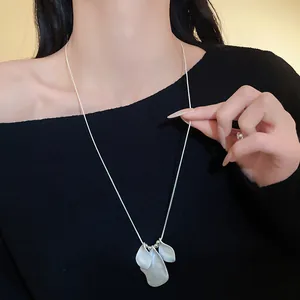 Close-up view of a silver irregular folded petal necklace pendant worn on black clothing