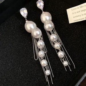 Close-up of long pearl tassel earrings with sparkling zircon studs on black background.