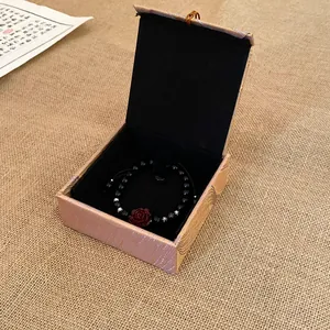 Elegant square fabric jewelry gift box featuring a black rose beaded bracelet on burlap background