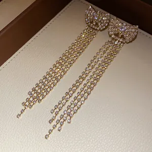 Close-up of sparkling zircon bowknot earrings with long hanging tassels in gold finish