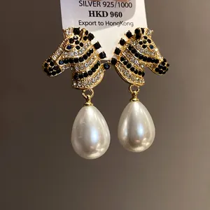 Close-up detail of zebra head earrings with sparkling zircons and white drop pearls