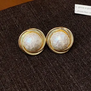 Primer plano de pendientes redondos vintage con perla de algodón texturizada y marco dorado