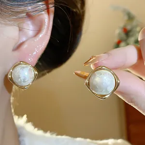 Vista detallada de pendientes de perlas de algodón bañados en oro usados en la oreja.