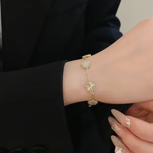 Detailed view of an elegant gold-plated flower charm bracelet worn on a wrist with black blazer