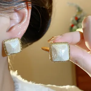 Vista macro detallada de pendientes cuadrados chapados en oro con perla de algodón