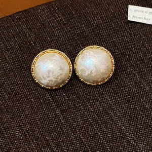 Detalle de pendientes redondos bañados en oro con elegantes perlas de algodón blancas.