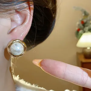 Elegante detalle de pendiente redondo bañado en oro con perla de algodón texturizada