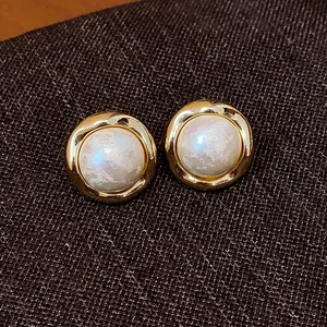 Primer plano de elegantes pendientes de botón redondos bañados en oro con perlas de algodón