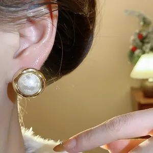Primer plano de elegantes pendientes redondos chapados en oro con perla de algodón texturizada