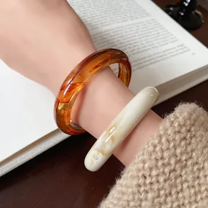 Close-up detail of irregular amber and cream resin bangles on wrist with knit sleeve