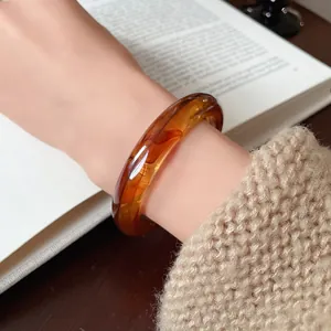 Detail of an amber-colored irregular resin bangle on a wrist with cozy knitwear