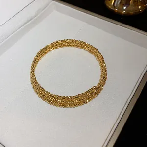 Dettaglio del bracciale rigido dorato a più strati con design a grana metallica irregolare.