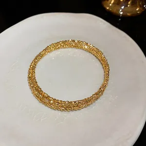 Dettaglio del bracciale in oro multistrato con trama metallica irregolare su piatto.