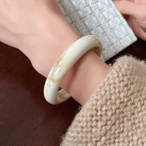 Detail of a marbled cream resin bangle with an irregular minimalist design worn on a wrist.