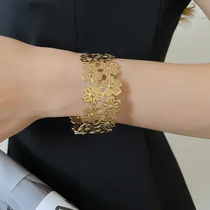 Detailed macro view of a wide gold metal floral cut-out bangle bracelet on a model's wrist.