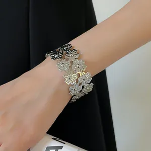 Detailed close-up of a silver-toned floral cutout metal cuff bracelet worn on a wrist