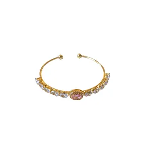 Elegant gold open bangle bracelet featuring a pink oval zircon and clear stones.