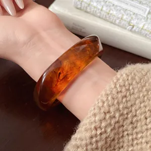 Close-up of irregular amber resin bangle with swirl patterns on a woman's wrist