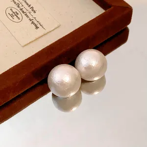Close-up of elegant cotton pearl earrings with a matte textured finish on a mirror.
