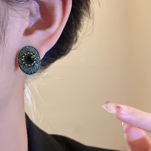 Close-up of vintage oval stud earring with emerald green and teal rhinestones on ear