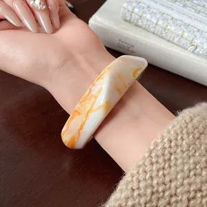 Close-up view of an irregular marbled resin bracelet with orange and white swirls on a wrist
