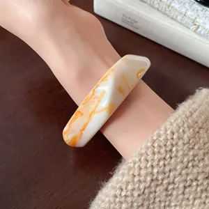 Close-up view of an irregular resin bangle with orange marble swirl texture on a wrist