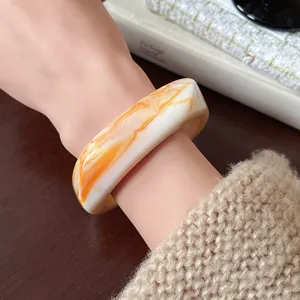 Close-up of irregular resin bangle with orange and white marble pattern on wrist