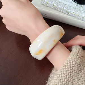 Detail shot of wide cream resin bangle with amber marble patterns on model's wrist