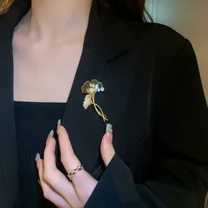 Detailed shot of a gold-plated ginkgo leaf brooch with pearl and zirconia on a black blazer.