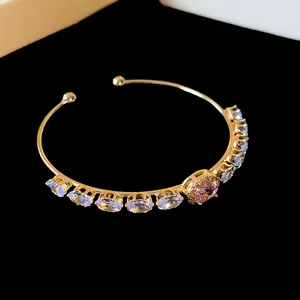 Close-up of a elegant golden open cuff bracelet with pink oval zircon and crystals