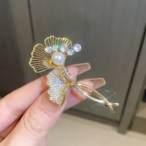 Close-up of gold-plated ginkgo leaf brooch with sparkling zircons and a central pearl.