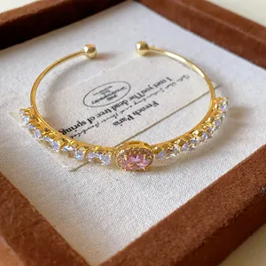 Close-up of elegant gold open cuff bracelet featuring a pink oval zircon center stone