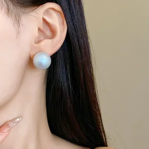 Close-up of large iridescent cotton pearl stud earrings with silver needles on ear.