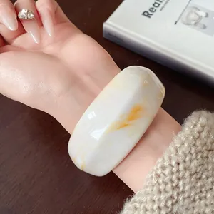 Detailed view of an irregular white resin bangle with amber marble patterns on a woman's wrist.