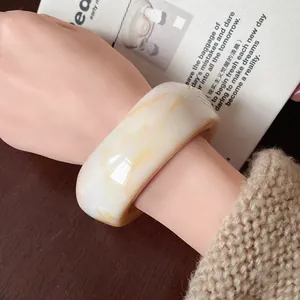 Detail view of thick irregular cream resin bangle with marble pattern on a wrist